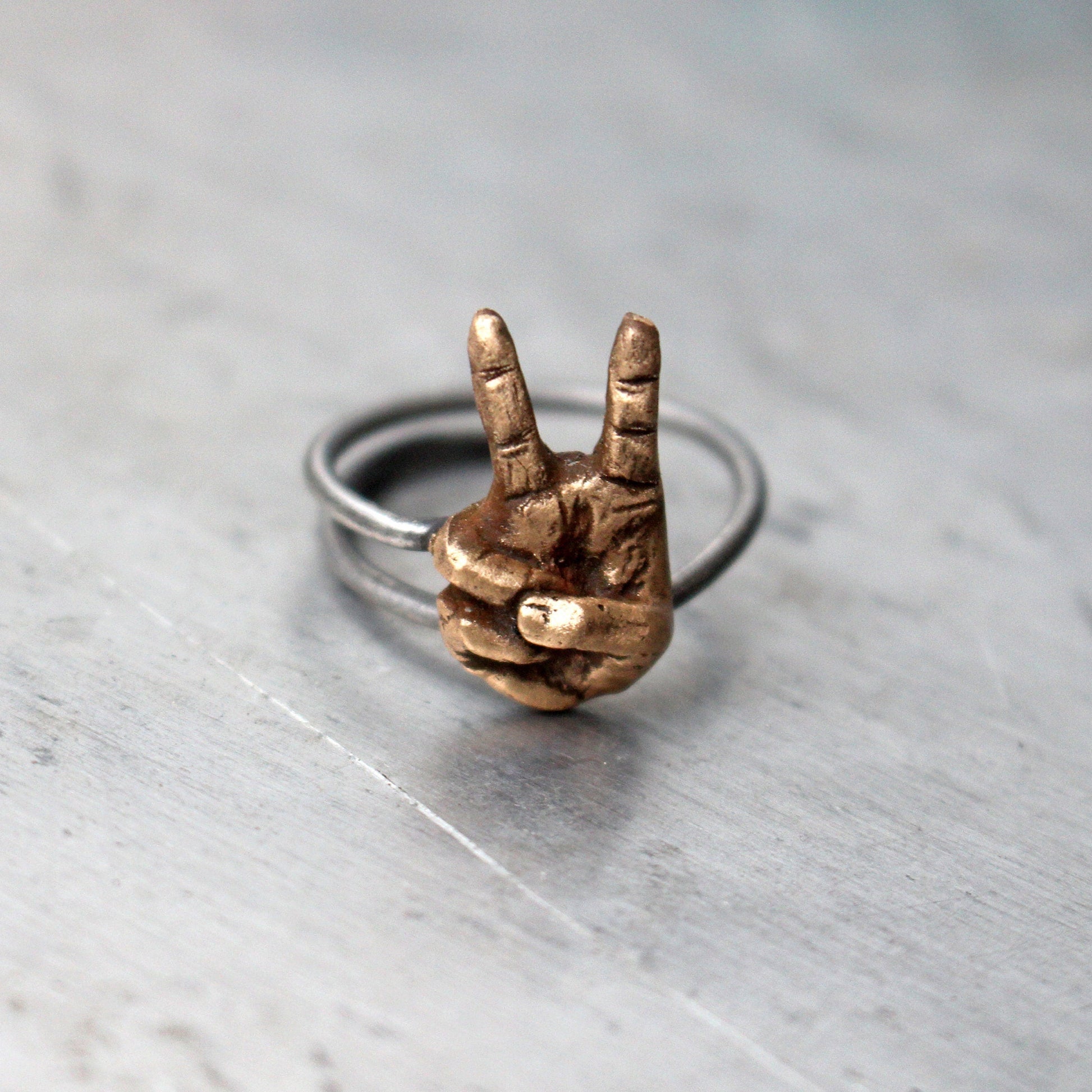 justerbar fingerring i brons och rostfritt stål med en miniatyrhand som gör segertecken eller fredstecken