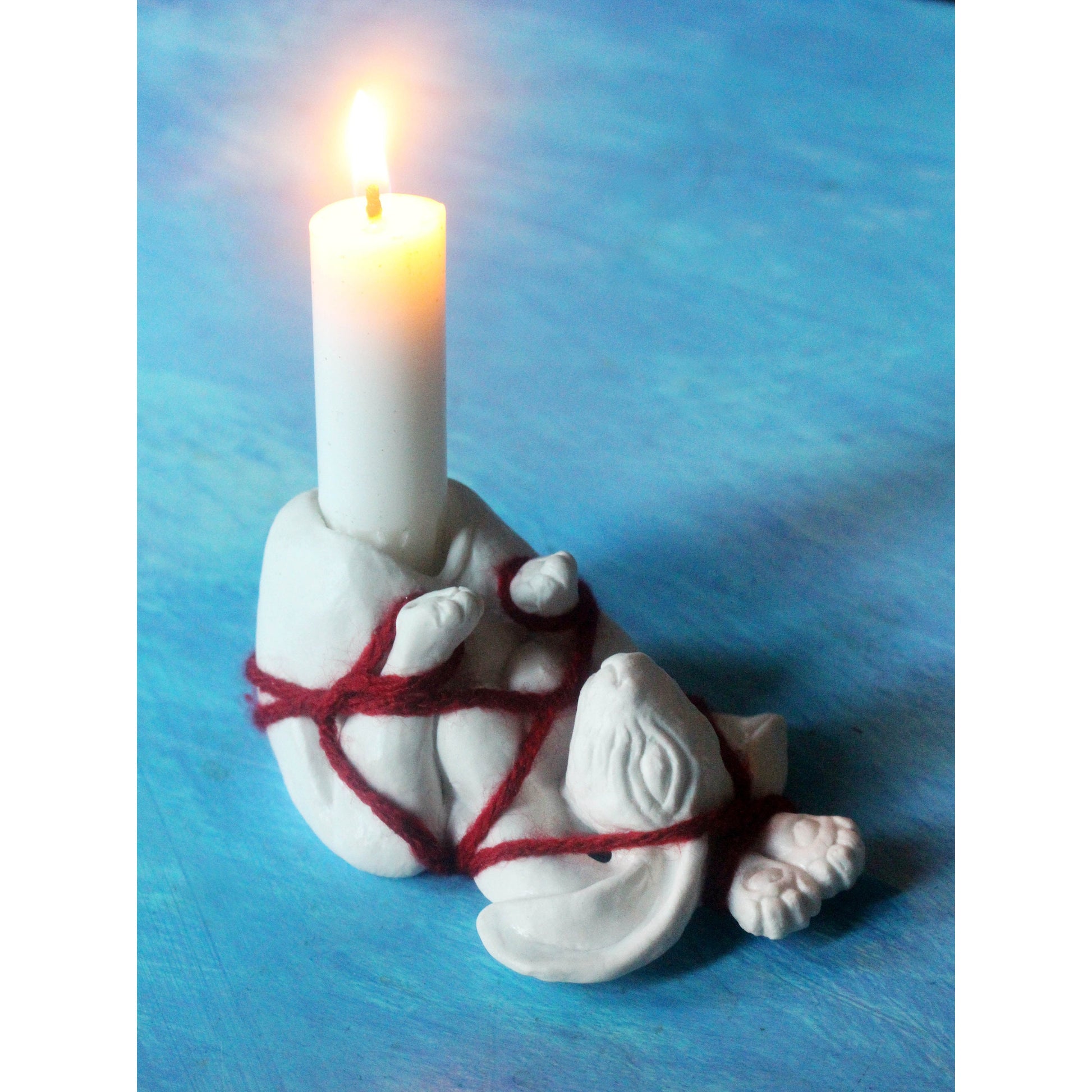 White porcelain figurine of a tied-up bunny with red yarn ropes, to be used as a candlestick 