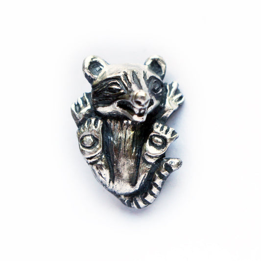 A silver pendant in the shape of a baby raccoon with detailed features, showcased on a plain background.