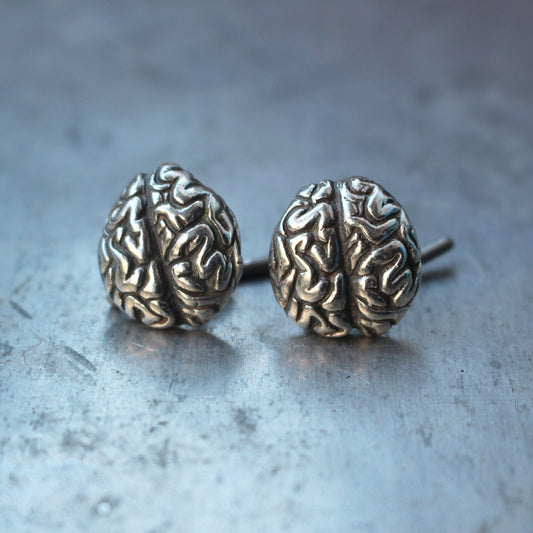 A pair of silver brain cufflinks with intricate detailing, displayed on a textured background.