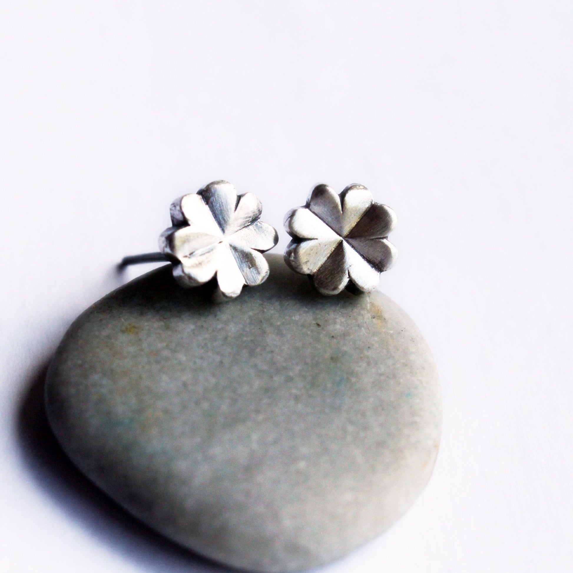 A pair of silver clover-shaped earrings placed on a stone.