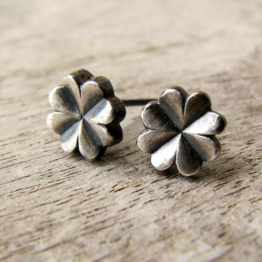 A pair of four leaf silver clover-shaped earrings placed on a wooden surface.
