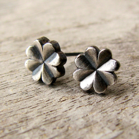 A pair of four leaf silver clover-shaped earrings placed on a wooden surface.
