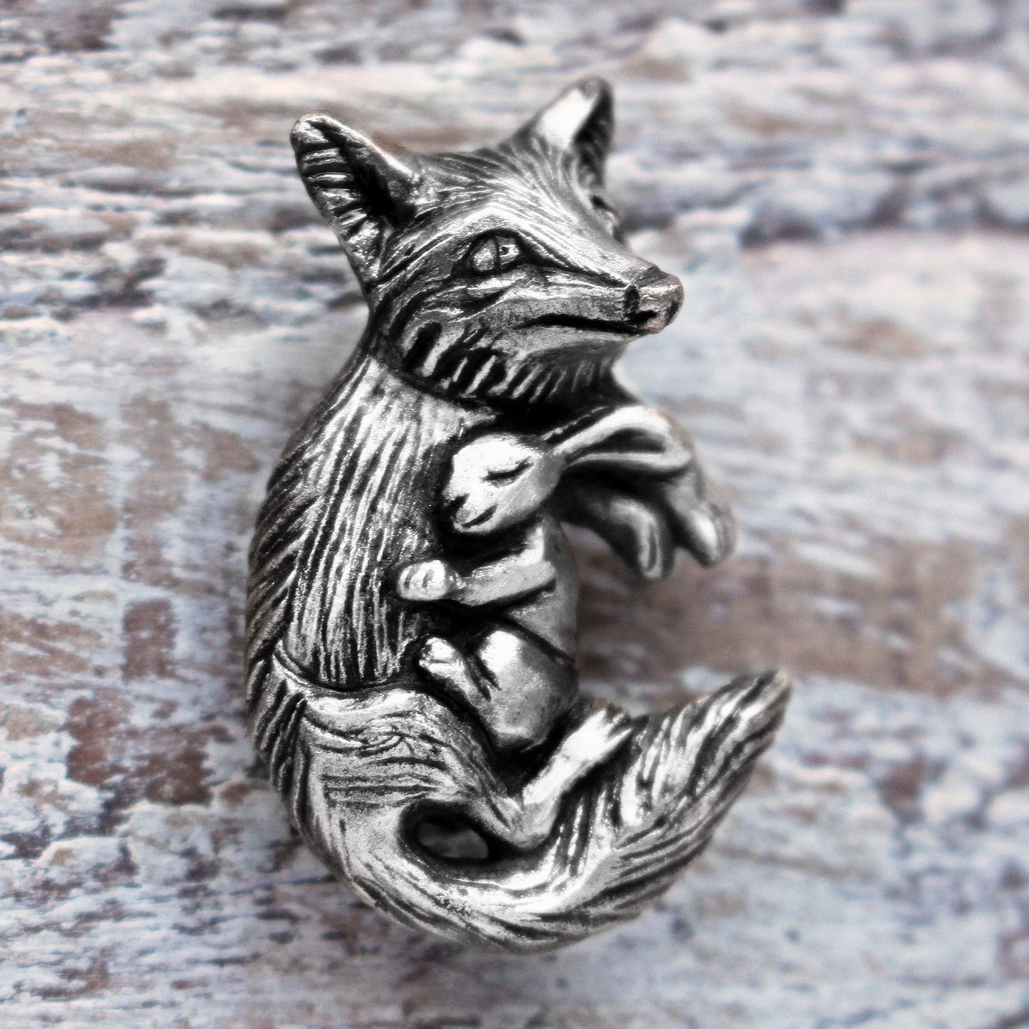 A silver necklace featuring a detailed fox and rabbit charm, displayed against a wooden background.