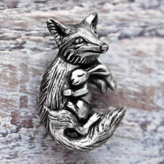 A silver necklace featuring a detailed fox and rabbit charm, displayed against a wooden background.