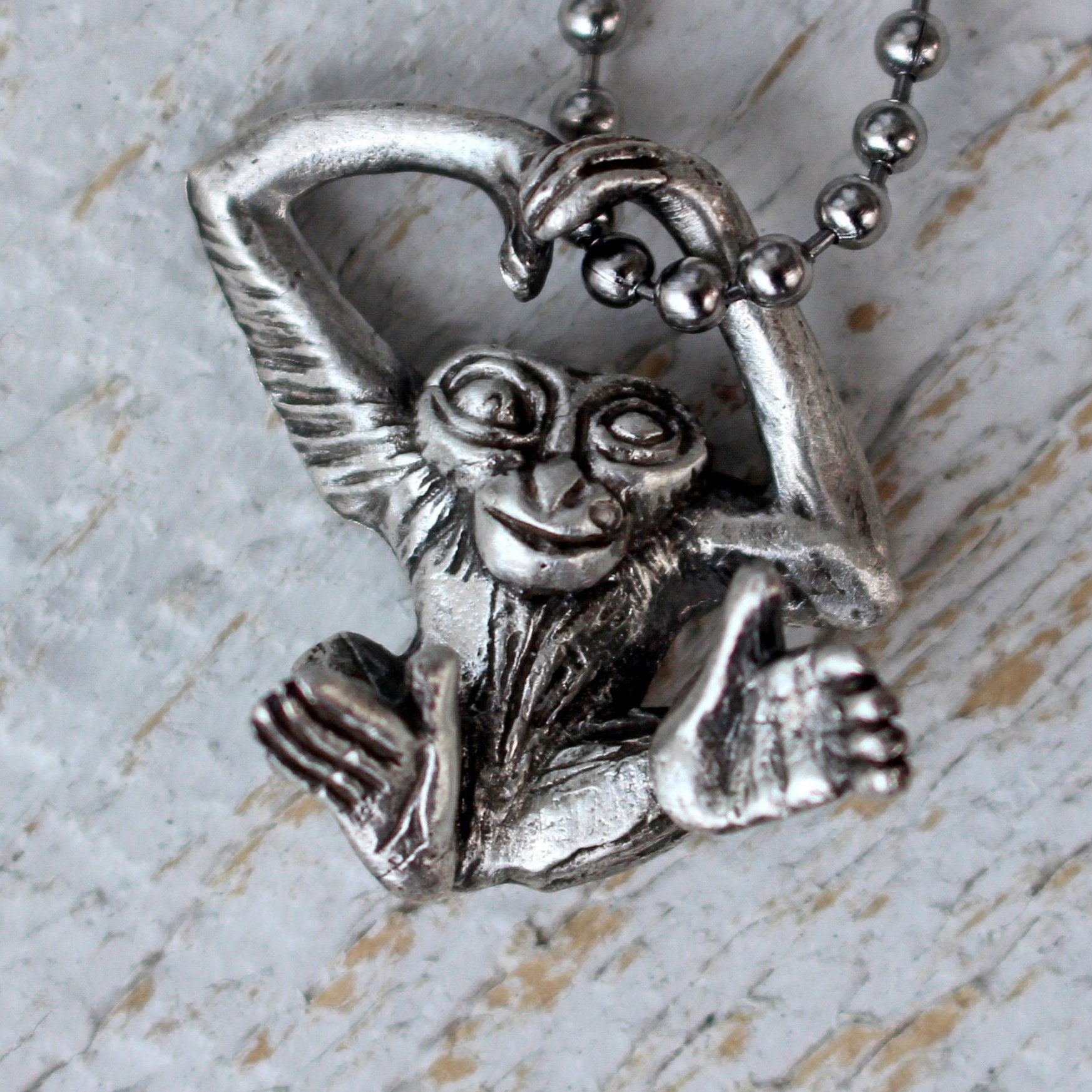 A silver necklace with a detailed miniature sculpture of a monkey swinging in the chain, crafted with focus on the monkey's feet and hands.