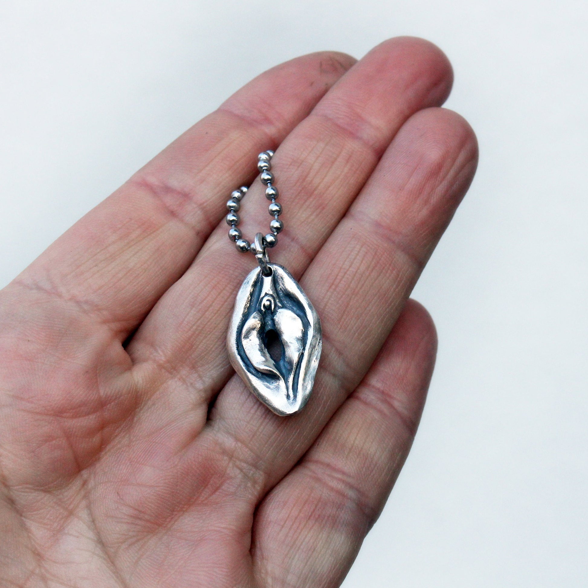 vändbart fitthalsband i sterling silver med en vulva på ena sidan och en mun på andra