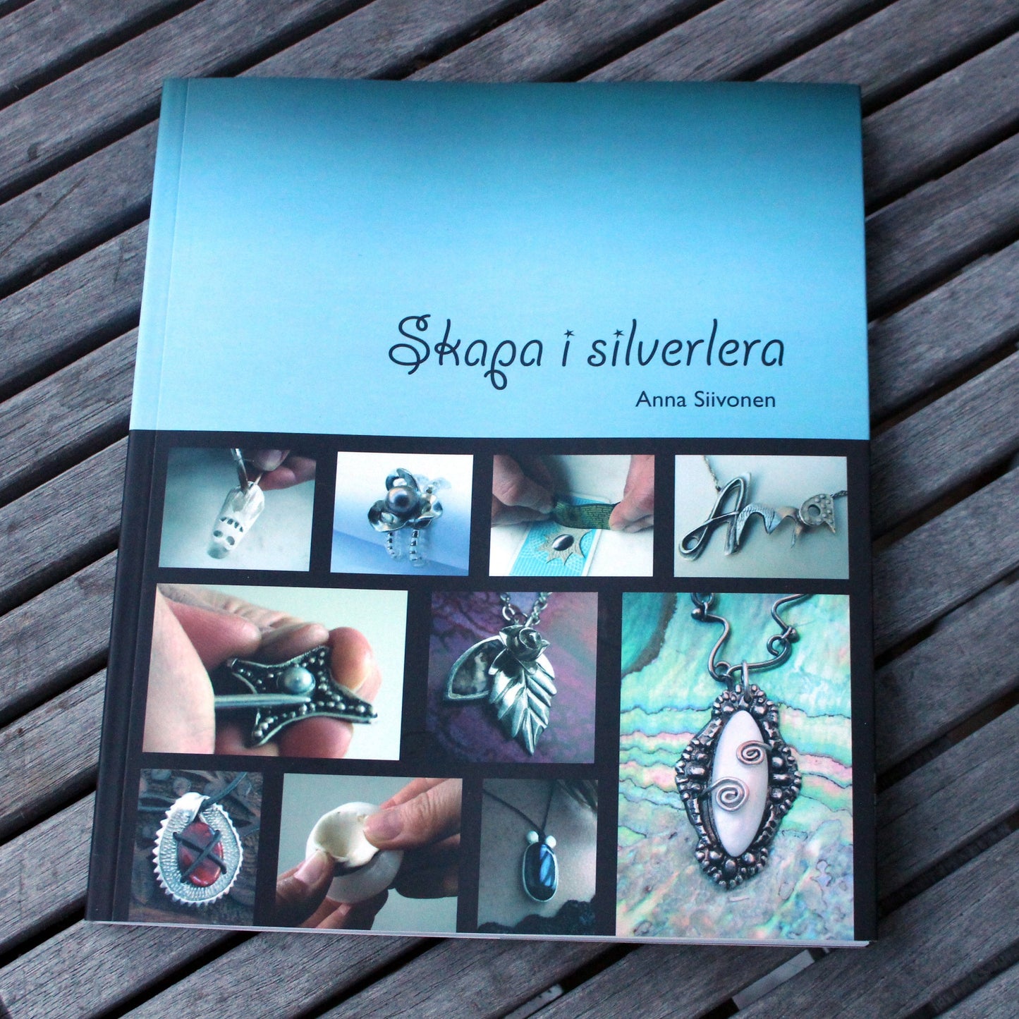 A book titled 'Skapa i silverlera' with a blue cover, showcasing various pieces of jewelry made from silver clay.