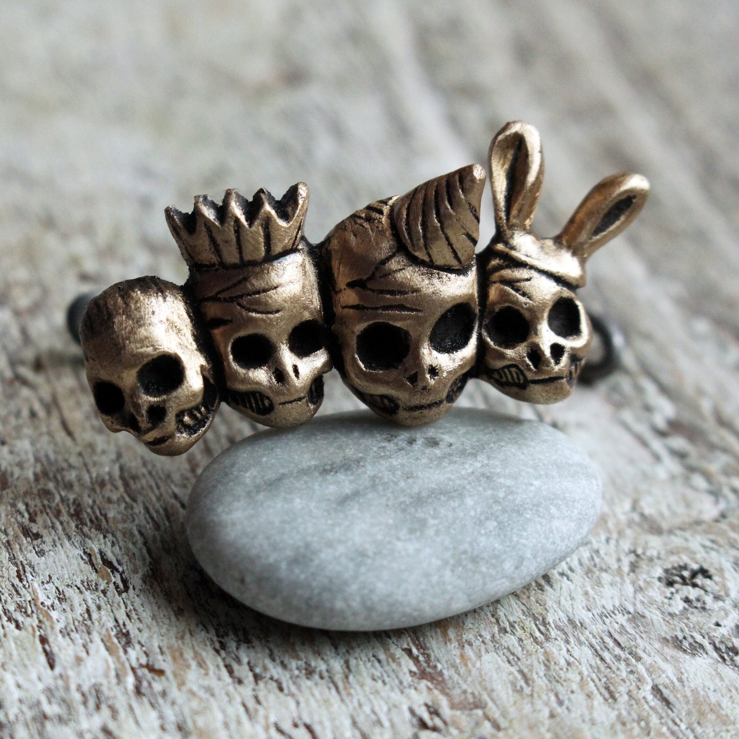 knuckle duster ring with four skull friends wearing party hats. bronze and steel