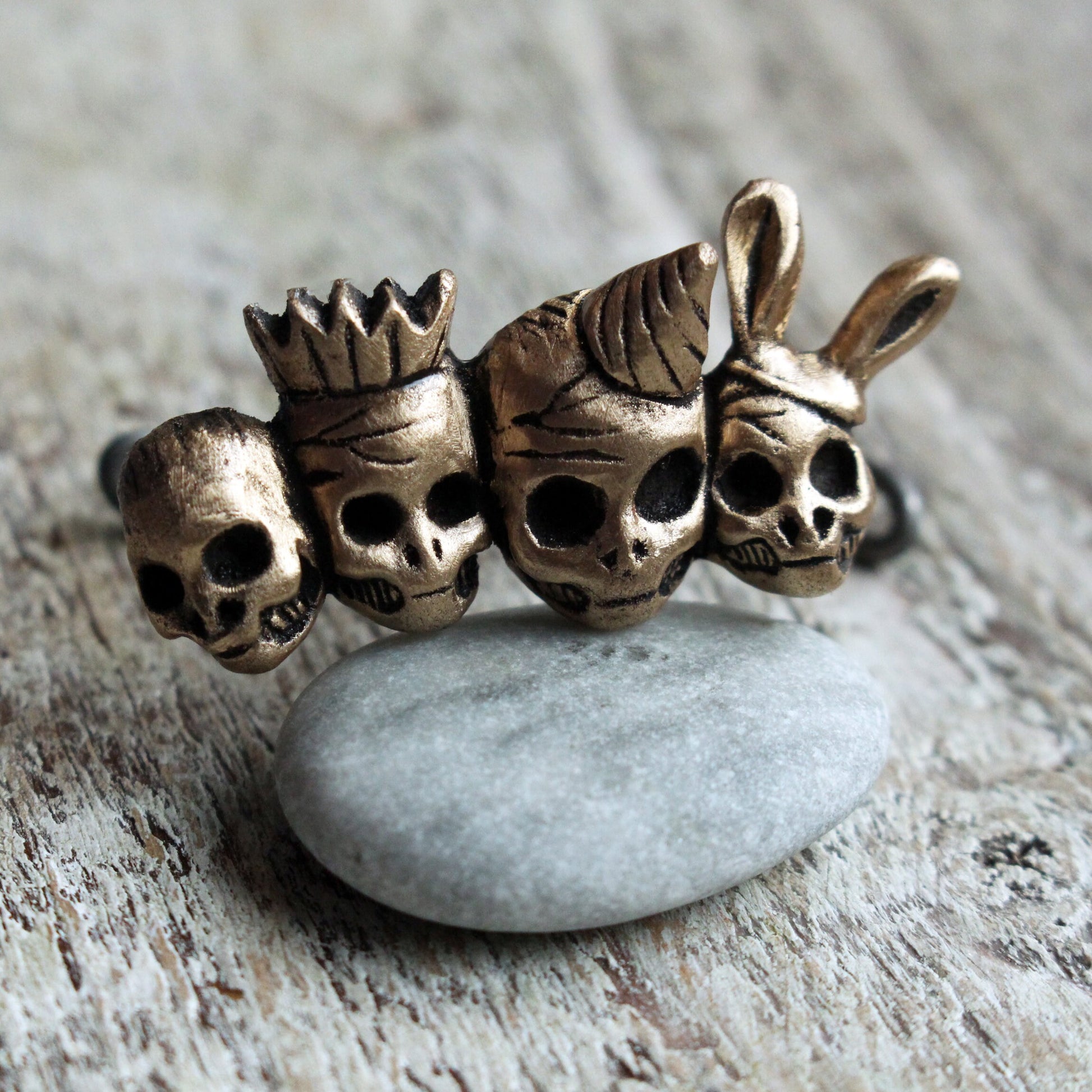 knuckle duster ring with four skull friends wearing party hats. bronze and steel