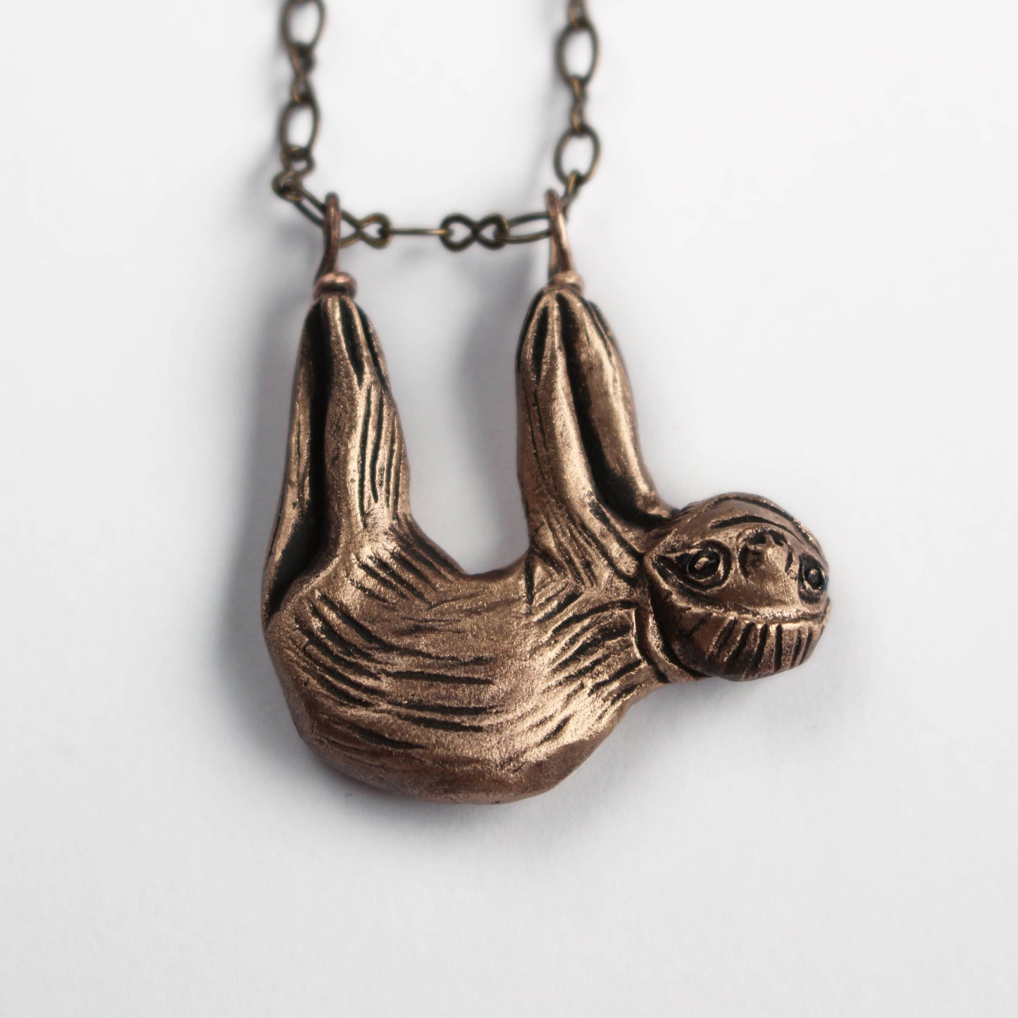 smiling sloth sculpted in bronze hanging in feets from a chain