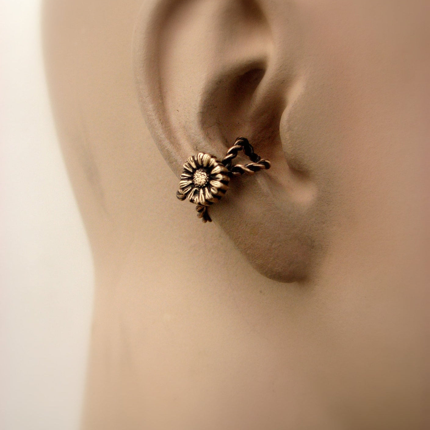earcuff med en solros skulpterad i brons, på modelldocka