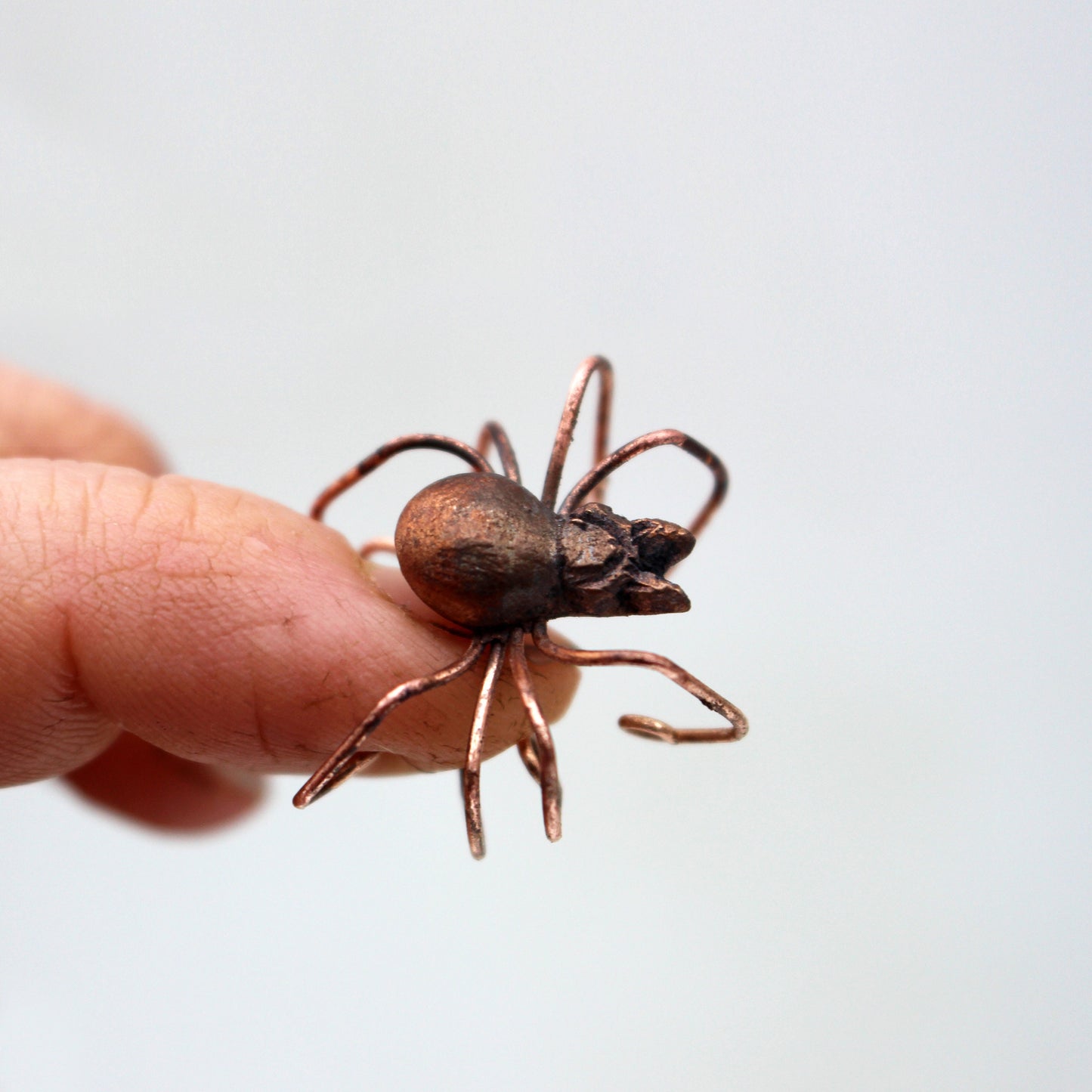 A bronze-colored spider ear cuff held between fingers, displaying its antiqued bronze look and wire frame design.