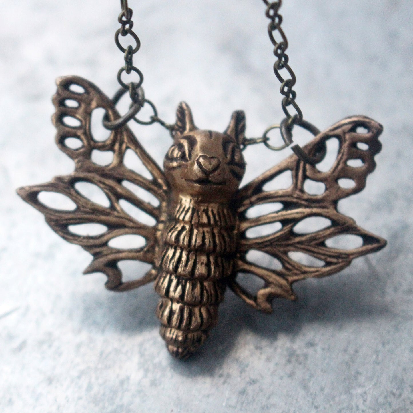 A bronze sculpture of a flying squirrel moth with outstretched wings, attached to a chain.
