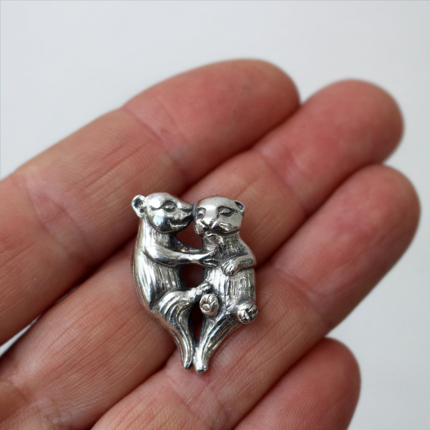 Silver necklace with a charm depicting two otters holding hands