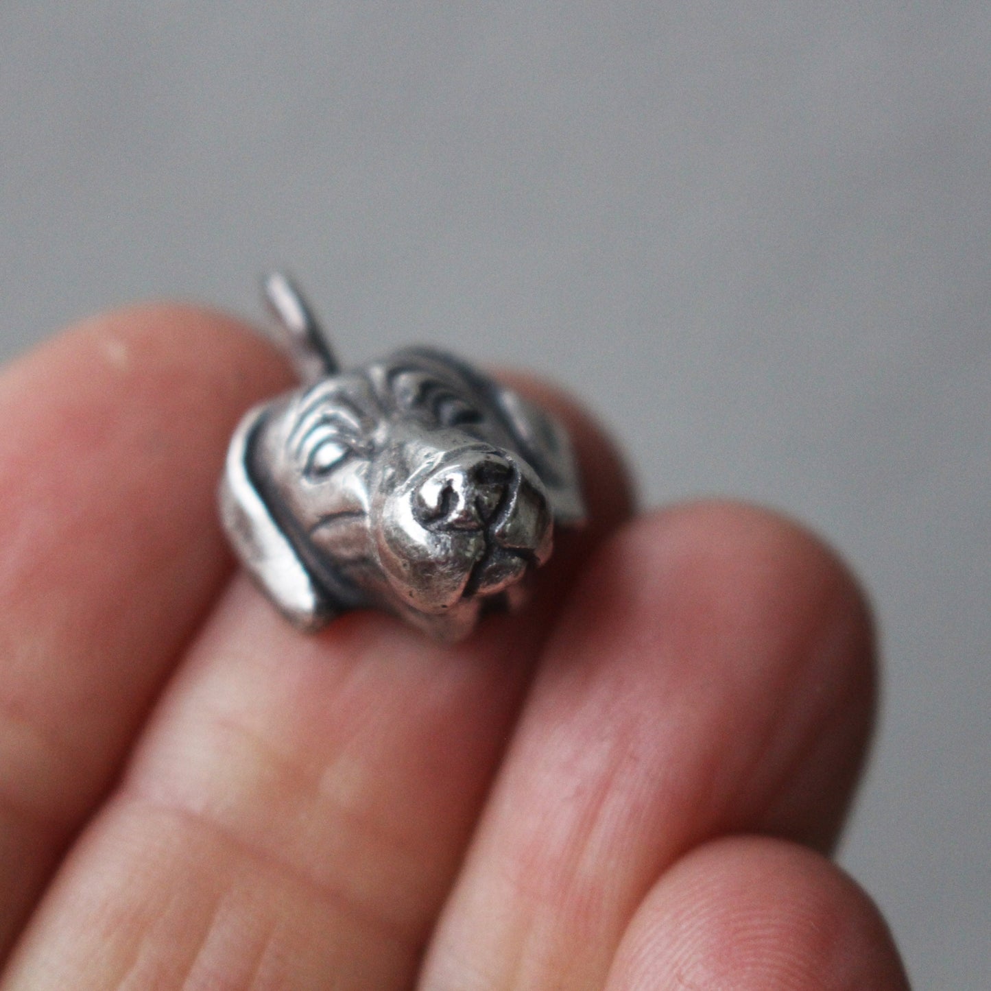 A sterling silver pendant in the shape of a Weimaraner dog head, held between fingers.