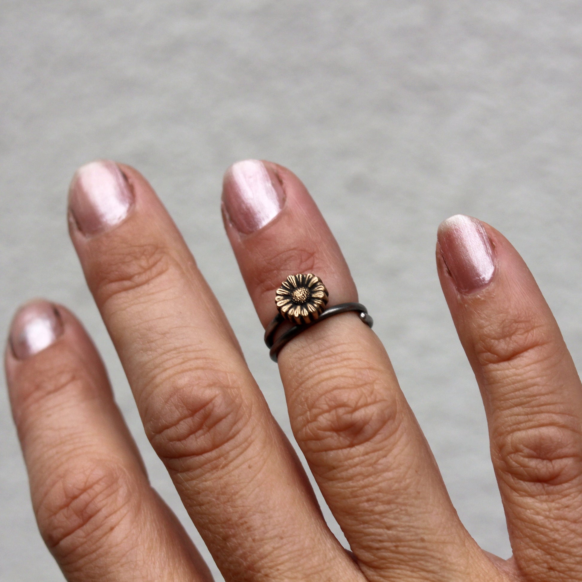 A bronze sunflower knuckle ring on a person's finger, with the ring's band adjusted to fit the finger comfortably.