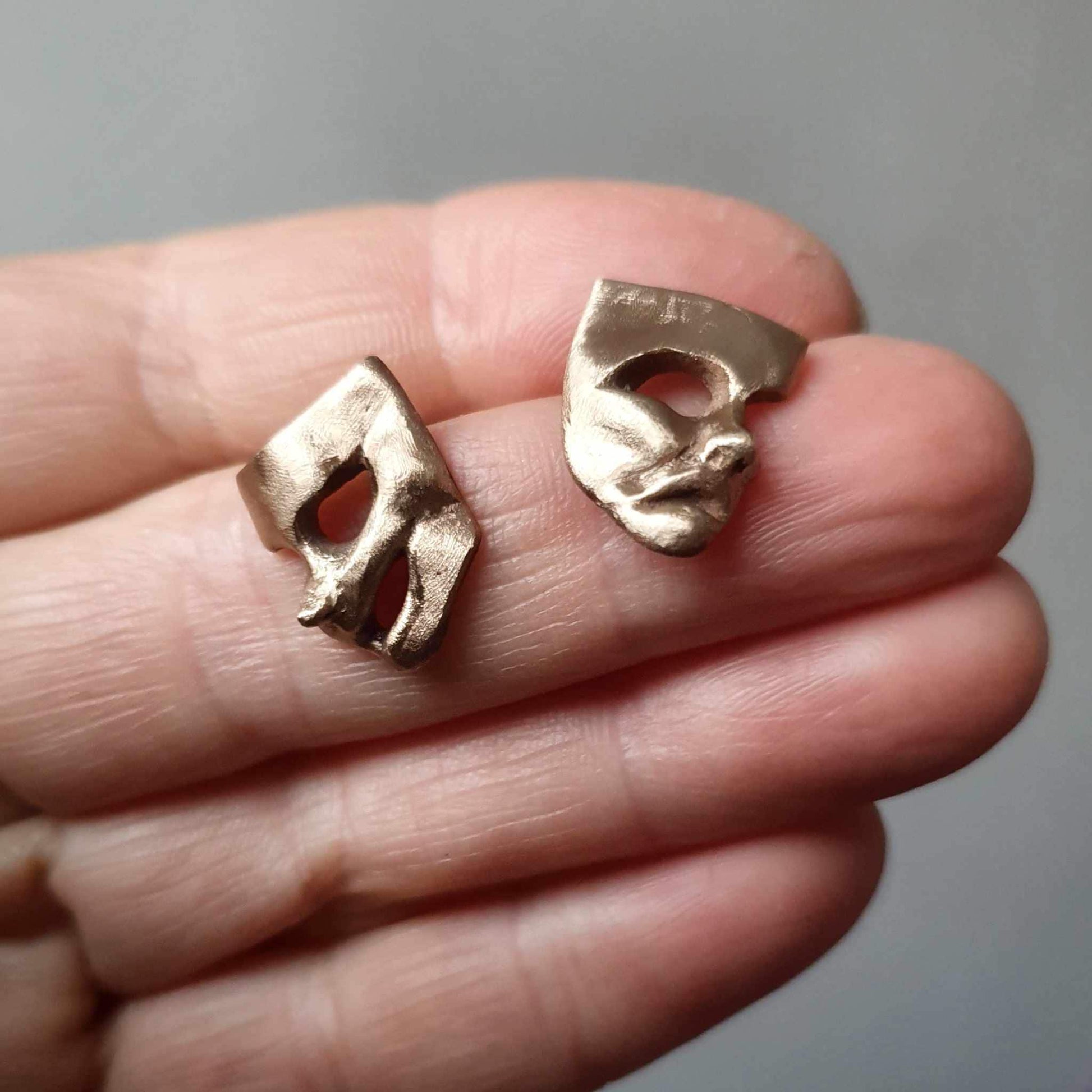 A pair of bronze theater mask earrings, one depicting a comedy mask and the other a tragedy mask
