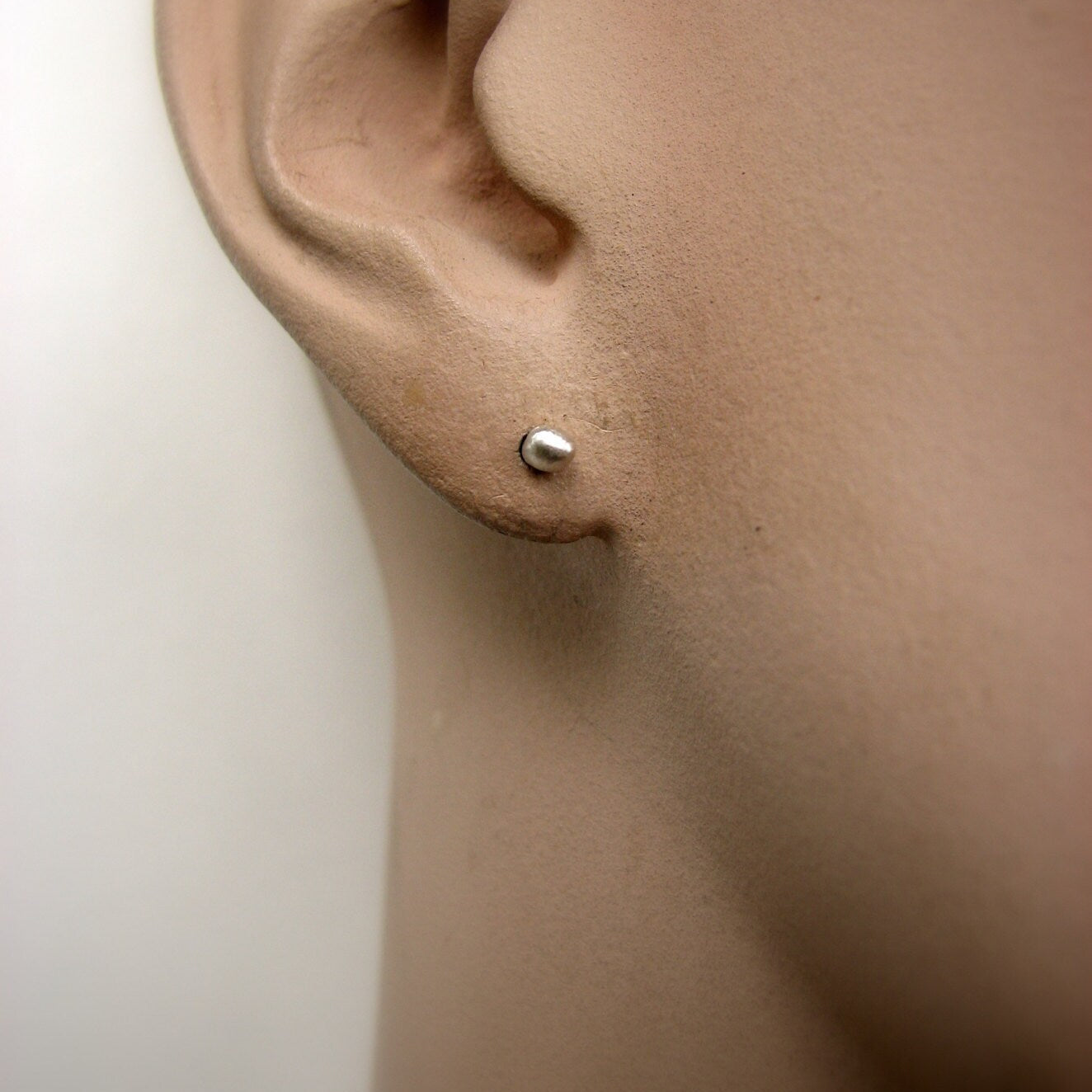 Close-up of an ear wearing a small silver earring on a neutral background
