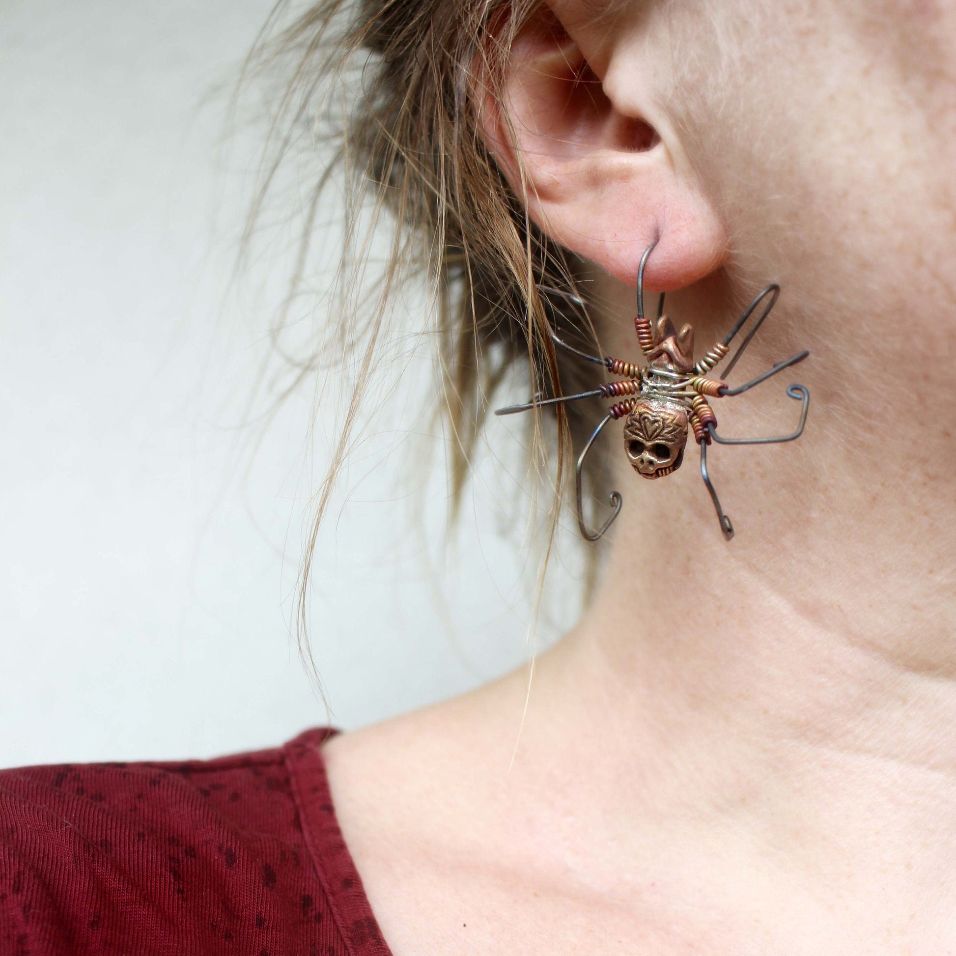 Large skull spider earring hanging from one leg piering an ear