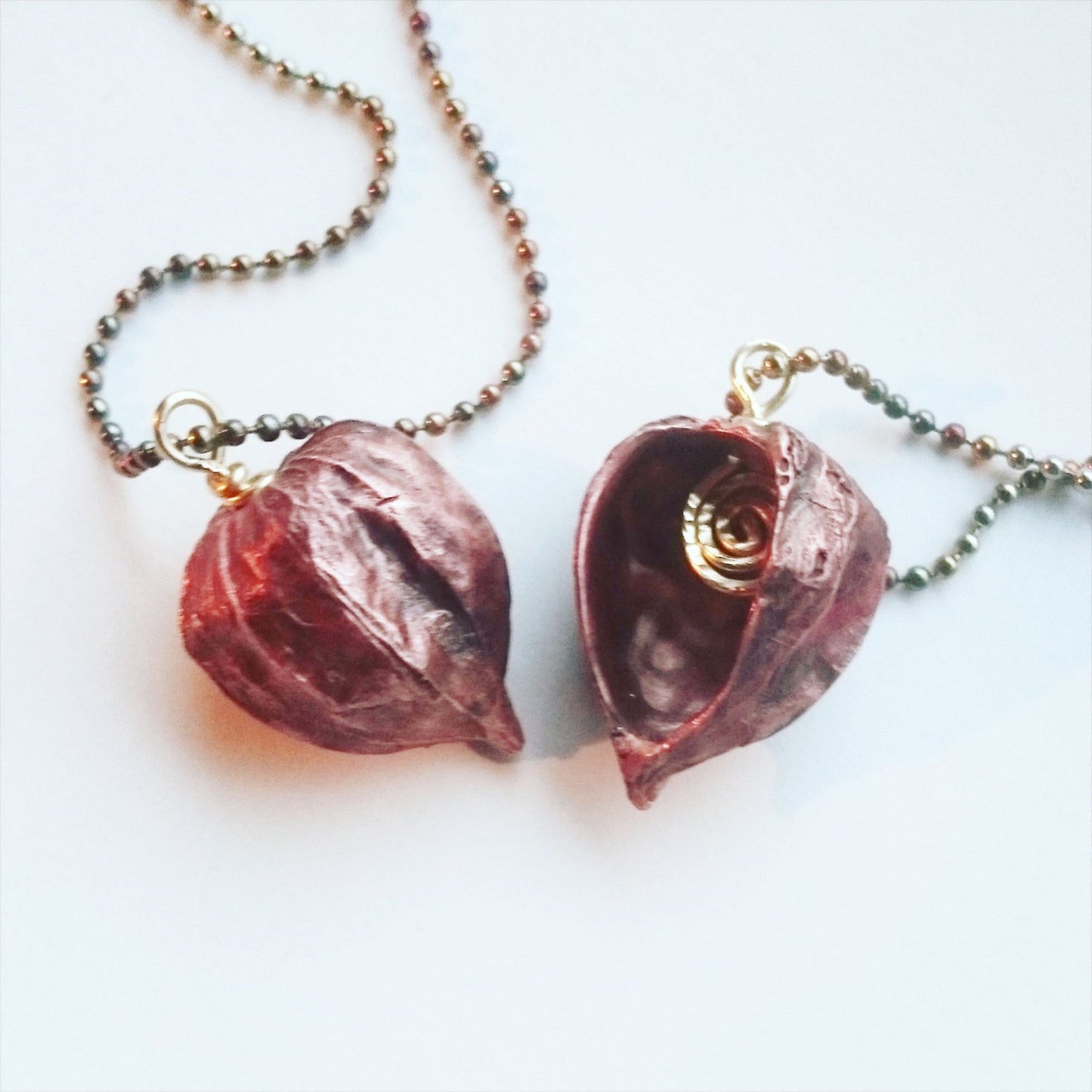 två physalis halsband, de är ihåliga och har en dekorativ smidd brons spiral inuti