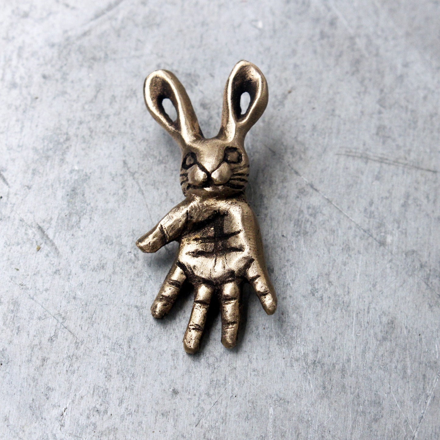 A bronze pendant depicting a small bunny creature with a hand design as a body