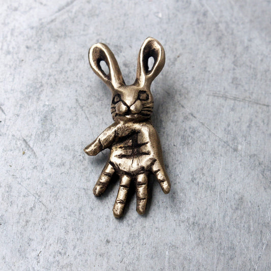 A bronze pendant depicting a small bunny creature with a hand design as a body