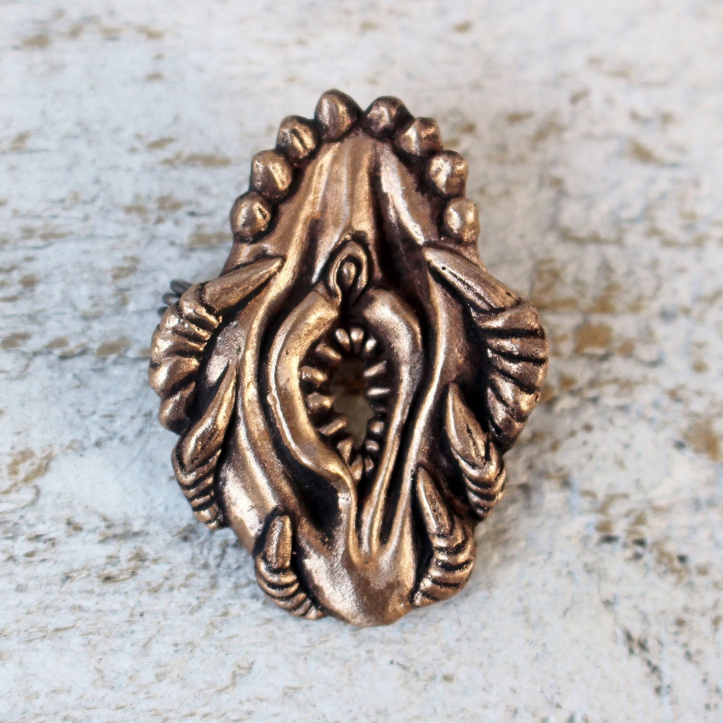 bronze brooch sculpted in the shape of a stylized female genitalia, with fangs and claws 