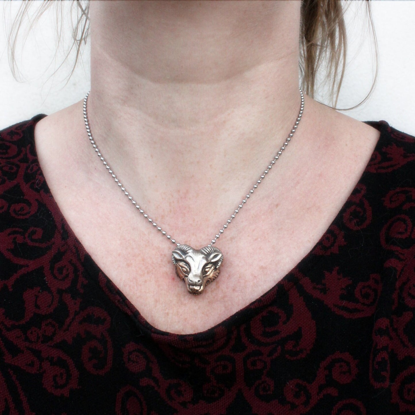 halsband med ett varghuvud i gul brons som bär en fårmask skulpterad i vit brons