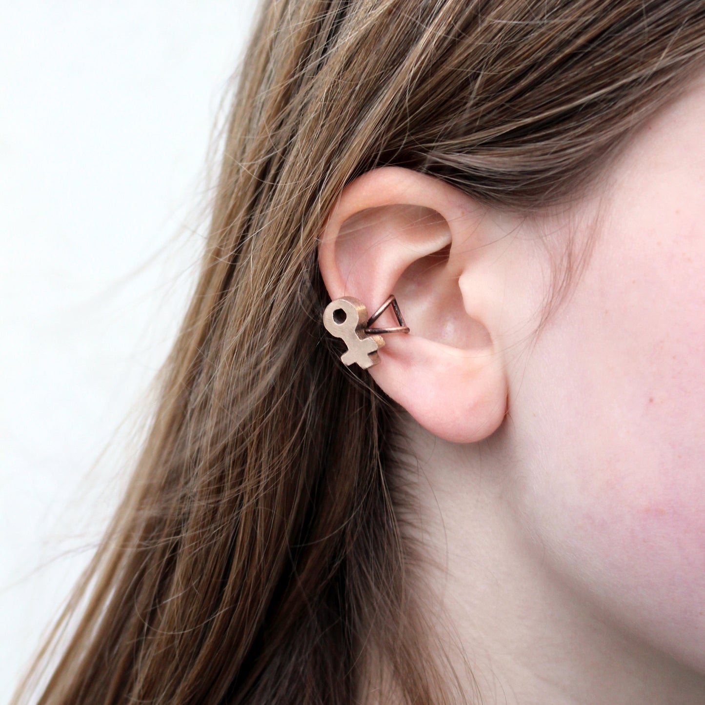 A person wearing a bronze ear cuff featuring the Venus symbol.