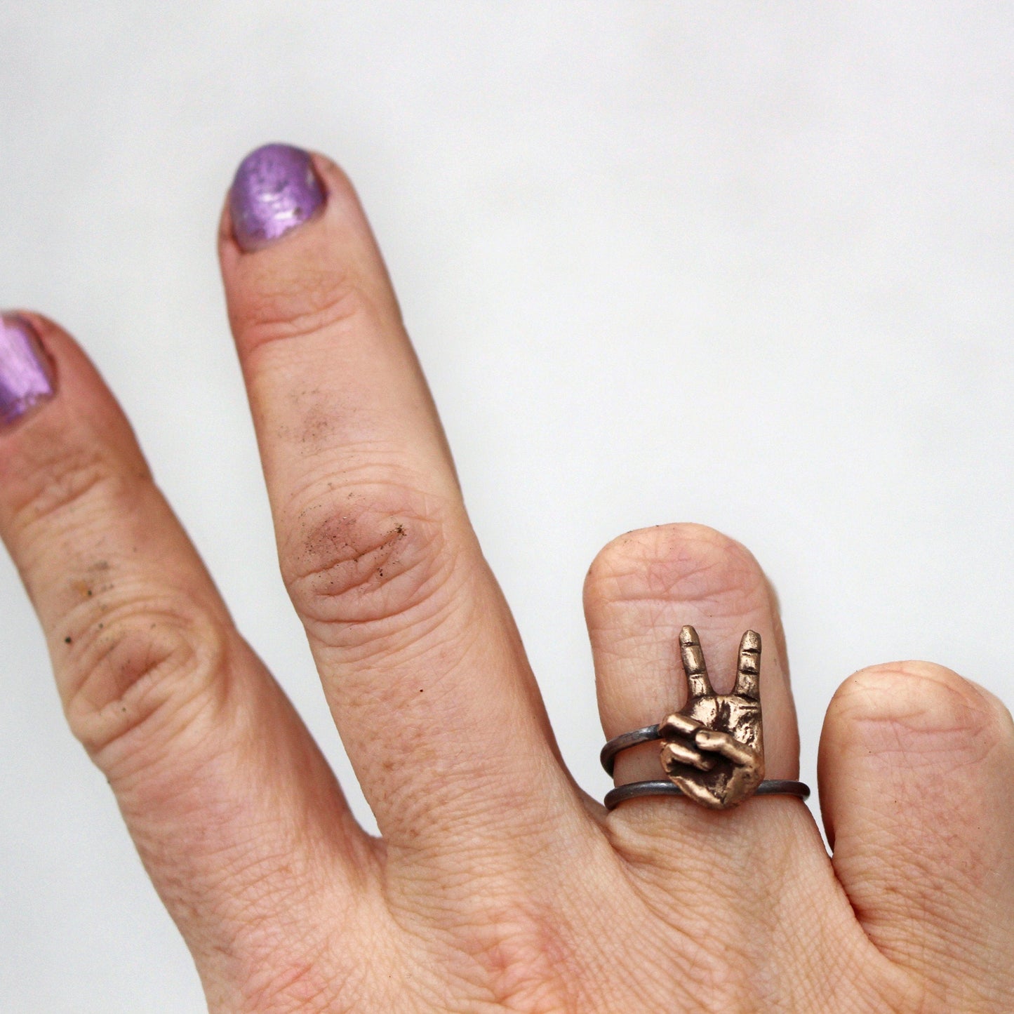 A hand displaying a ring with a detailed bronze hand making the peace sign