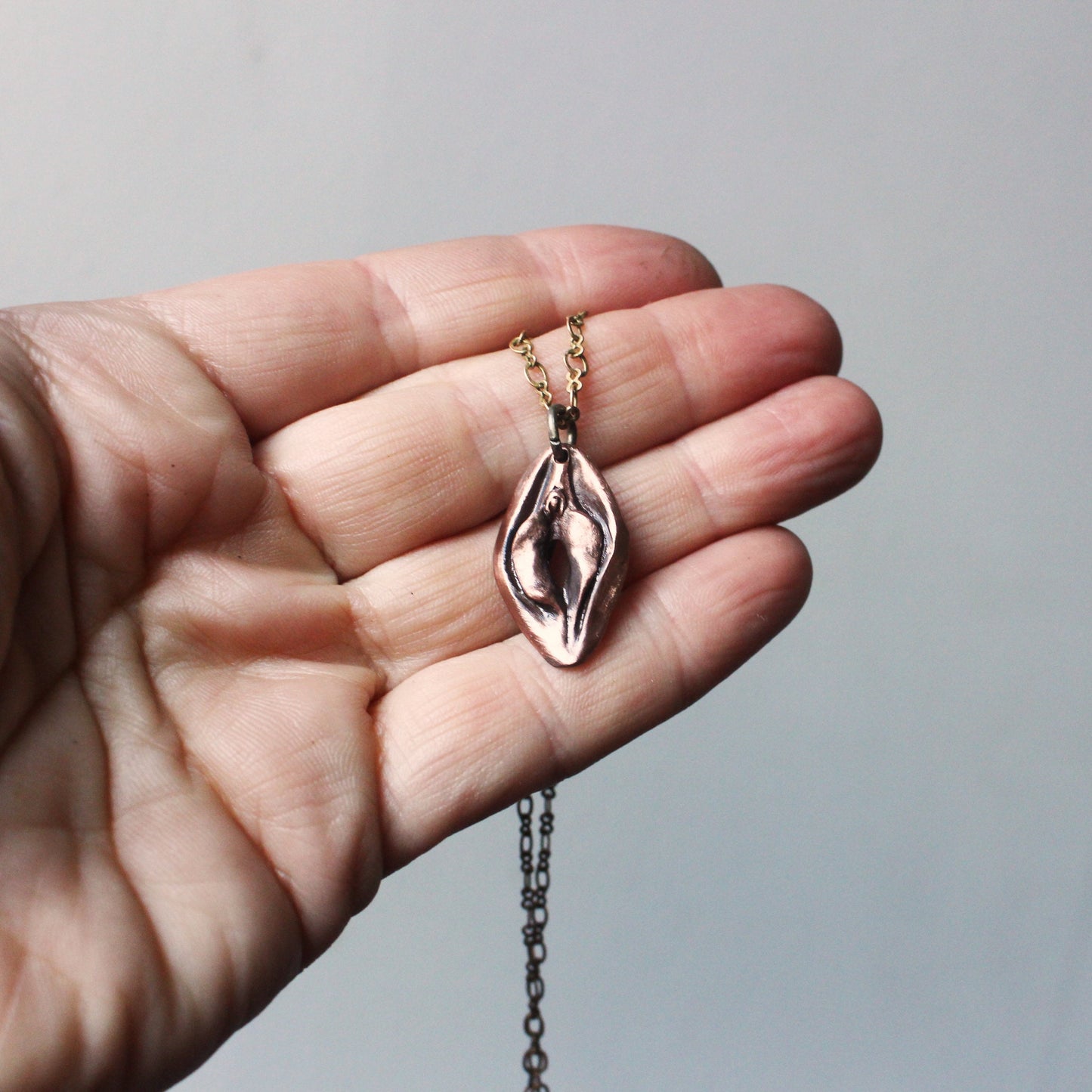 vändbart feminist smycke i koppar med en fitta på ena sidan och en mun på andra