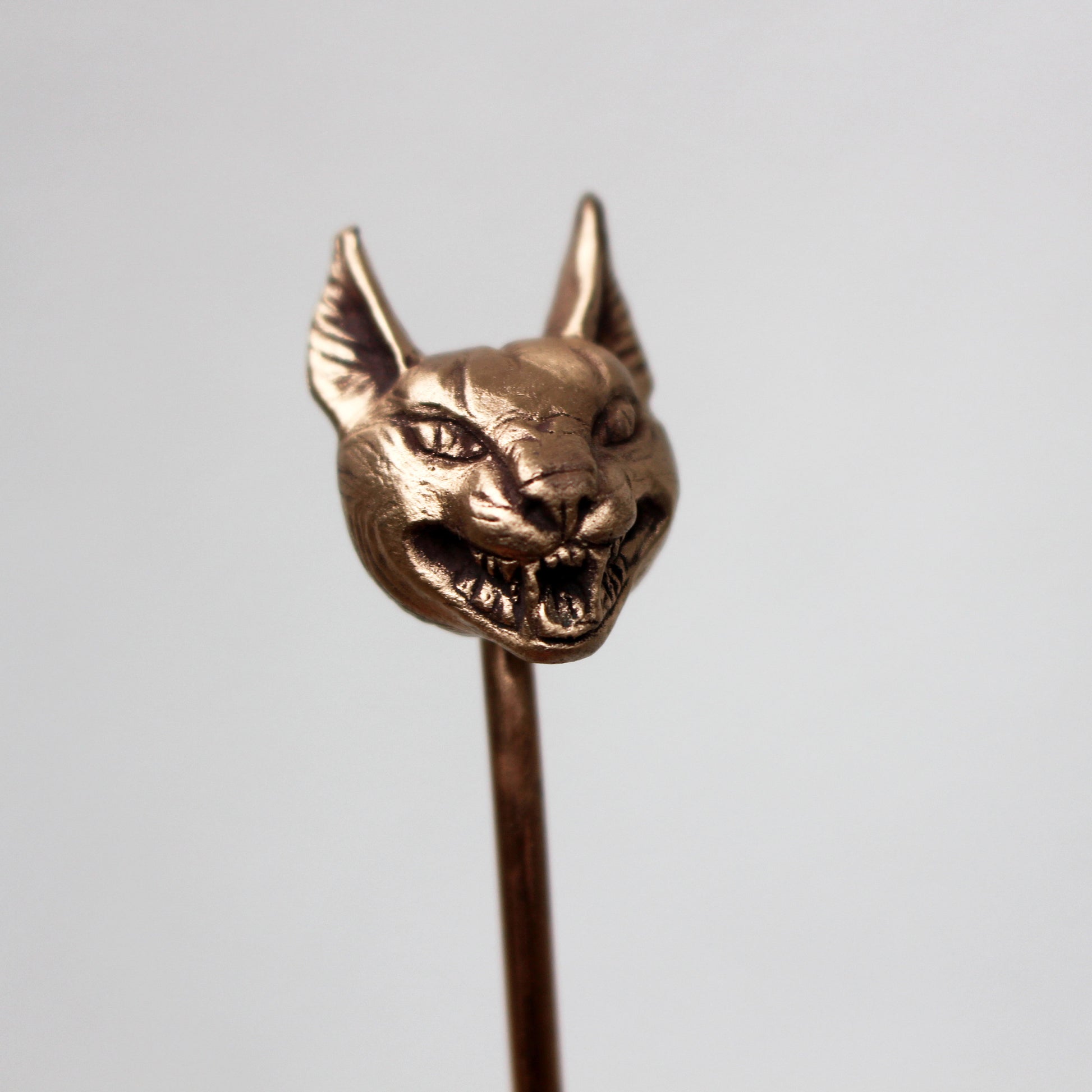 A bronze hair stick with a sculpted wild cat head at the top, displayed against a light background.