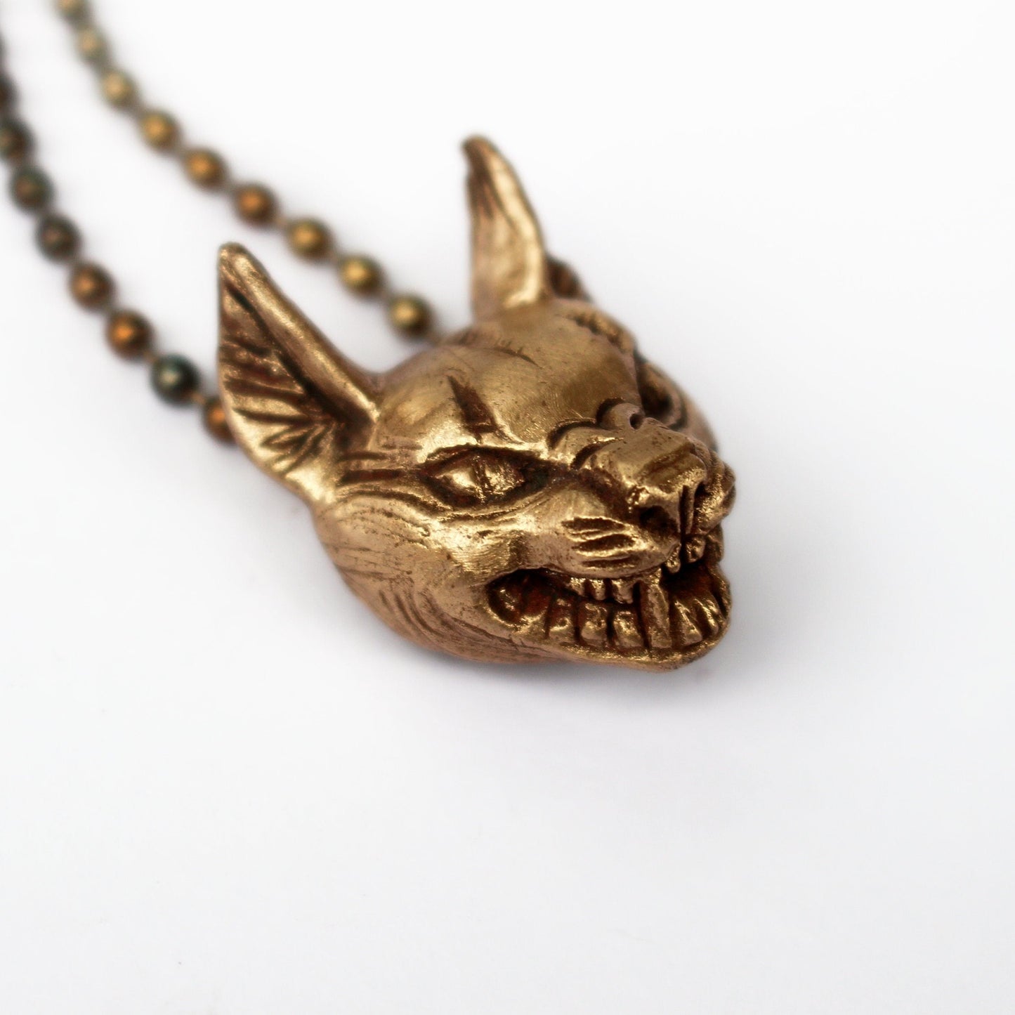 Bronze charachal cat head pendant on a chain against a white background