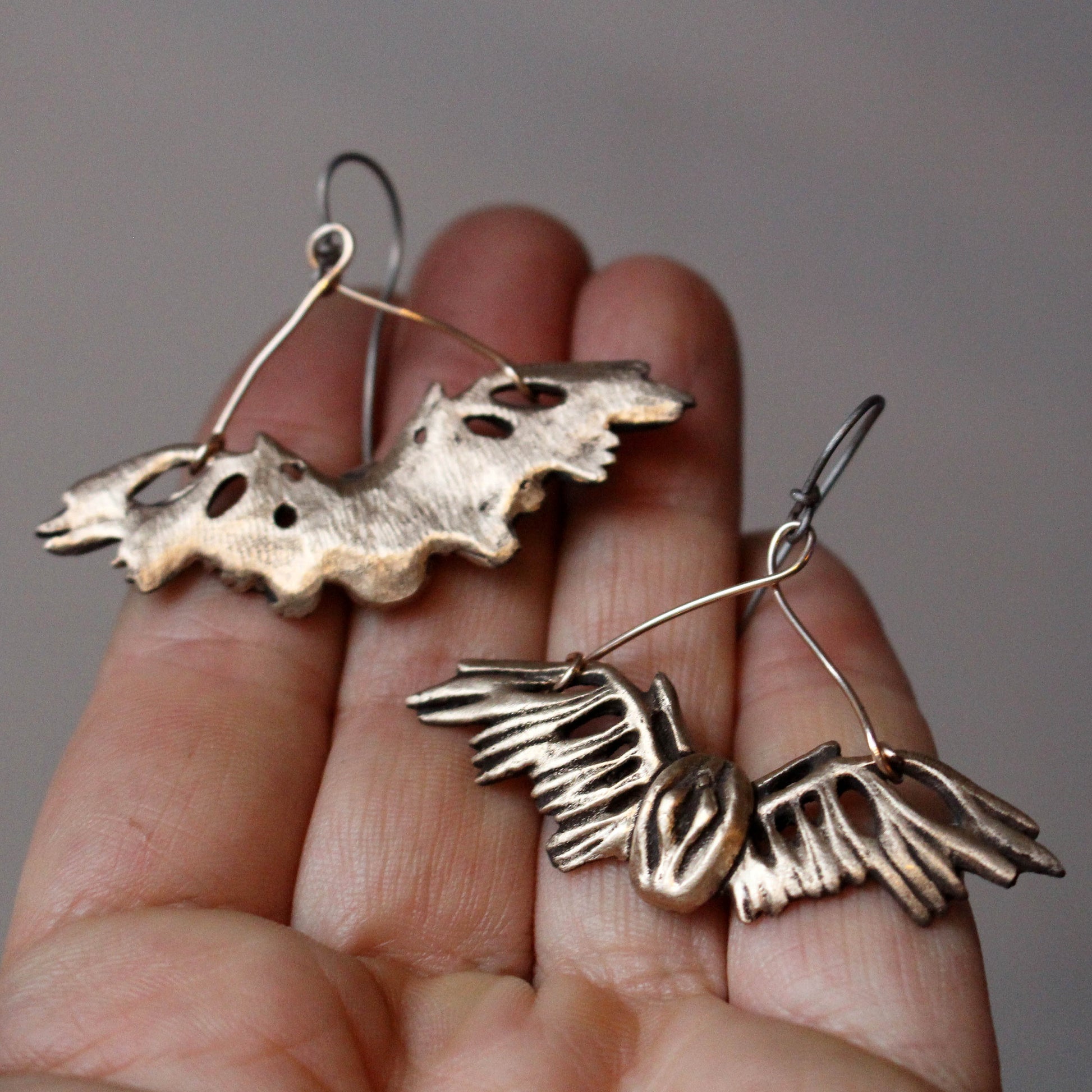 a pair of distinctive earrings featuring winged pussys, female genetalia,  Crafted from bronze with titanium wire hooks