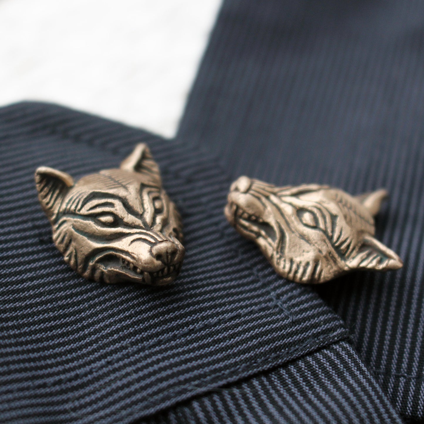 A pair of bronze wolf head cufflinks on a striped fabric surface.