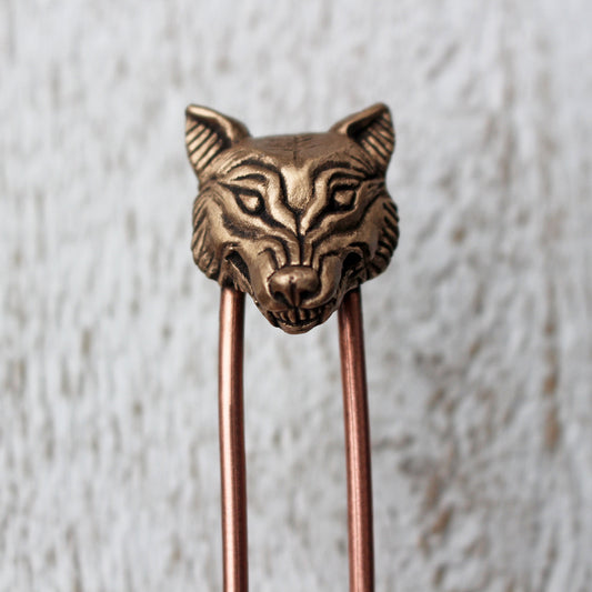 A bronze hair fork with a sculpted wolf head on the top, with two copper rods extending downwards.